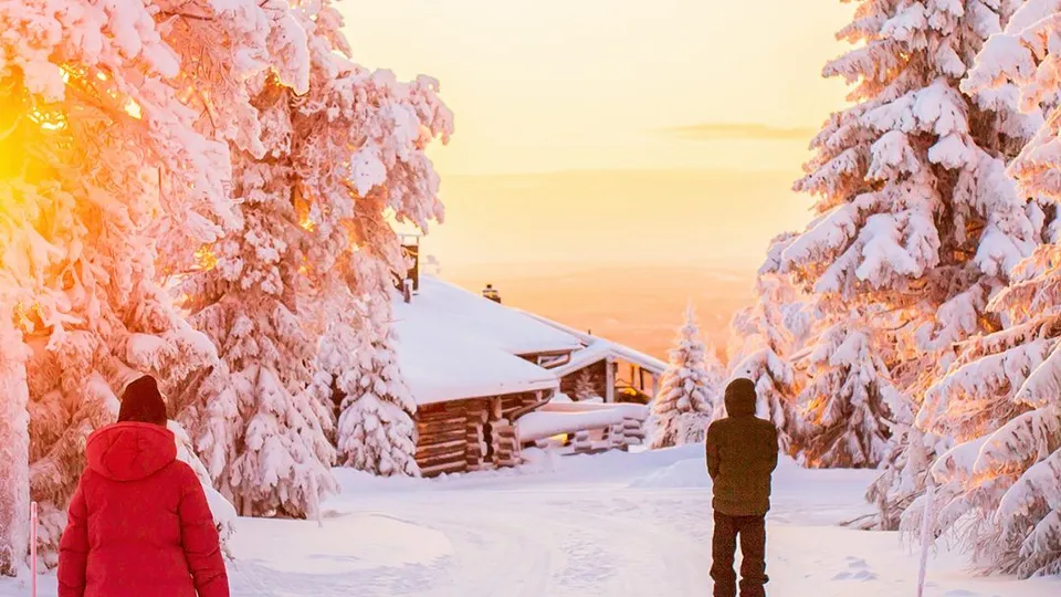 Paesaggio innevato con persone, alberi e case al tramonto